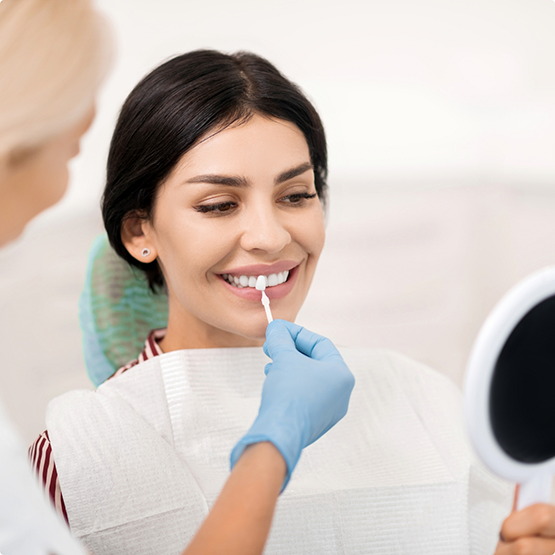 Dentist holding a veneer in front of a patient's smile