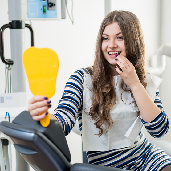 Young woman in the dental chair looking at her smile in a mirror