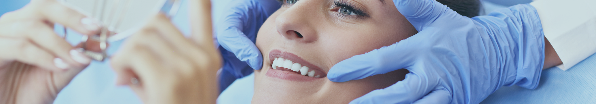 Woman looking at her smile in a mirror after receiving dental services in Tewksbury
